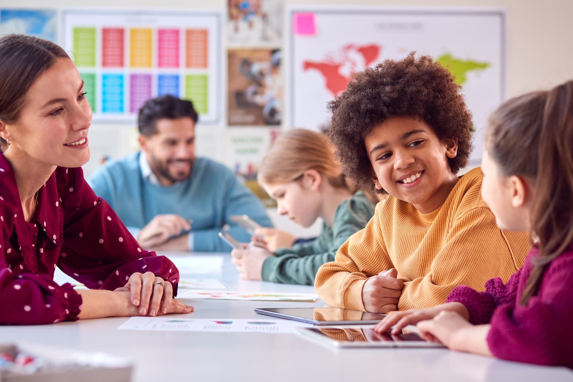 Teacher supporting primary school students using tablets during a classroom learning activity.
